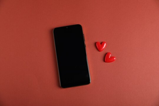 Online dating site. Smartphone and hearts on red-brown background, flat lay