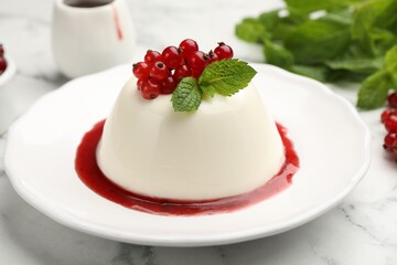 Delicious panna cotta with red currants, sauce and mint on white marble table, closeup