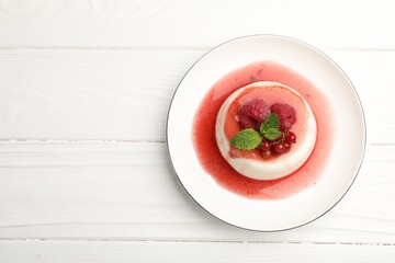 Delicious panna cotta with berries, sauce and mint on white wooden table, top view. Space for text