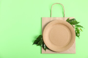 Eco friendly packaging. Paper bag, plate and leaves on light green background, top view. Space for...