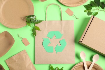 Recycling symbol, different eco friendly packaging and leaves on light green background, flat lay
