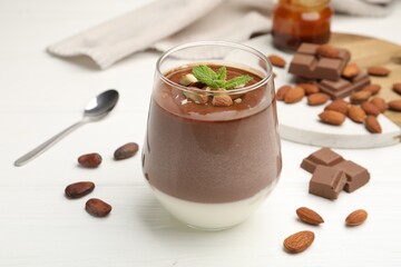 Delicious chocolate panna cotta with almonds, mint and cocoa beans on white wooden table, closeup