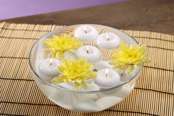 Burning candles and flowers in bowl of water on wooden table, closeup