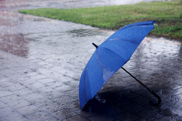 Blue umbrella on wet asphalt under heavy rain, space for text