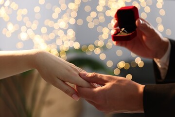 Man with engagement ring making marriage proposal to his girlfriend indoors, closeup. Bokeh effect