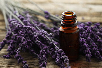 Lavender essential oil in bottle and flowers on wooden table, closeup