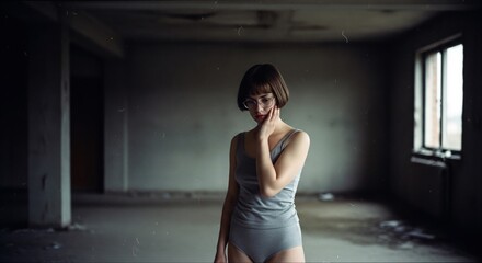 Young thoughtful woman with short haircut and glasses, wearing gray underwear, posing in abandoned building, reflecting on past and future, captured in moody, atmospheric light .
