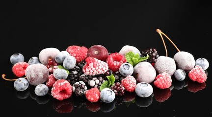 Many different frozen berries and mint on black table