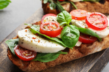 Delicious sandwich with mozzarella cheese, tomato and basil on table, closeup