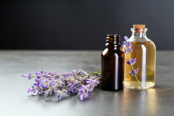 Aromatic essential oil in bottles and lavender flowers on grey textured table against dark background, closeup
