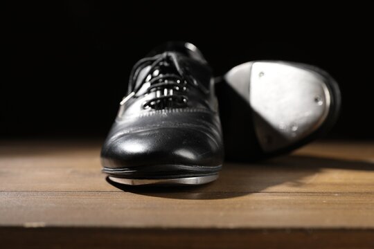 Pair of tap shoes on wooden floor against black background, closeup. Tap dance