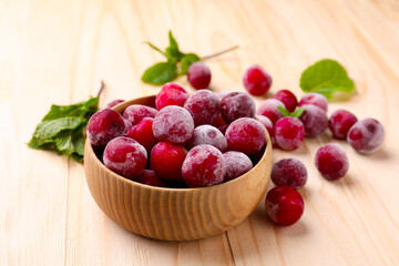 Ripe frozen cherries and bowl on light wooden table, closeup