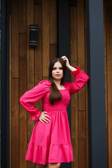 The girl is leaning one hand on a vertical dark column, and the other hand is placed on her waist.