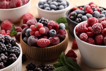 Different ripe frozen berries and mint leaves on light wooden table, closeup