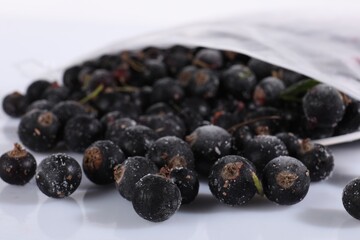 Ripe frozen black currants in open zipper bag on mirror surface against white background, closeup