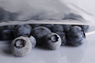 Ripe frozen blueberries in open zipper bag on white mirror surface, closeup