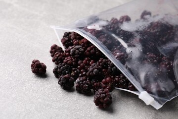 Ripe frozen blackberries in open zipper bag on grey textured table, closeup