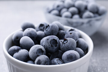 Ripe frozen blueberries in bowl on grey table, closeup