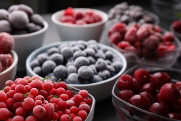 Different ripe frozen berries in bowls on table against black background, closeup