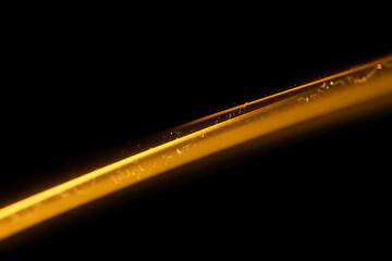 Close up macro shot of a single golden hair strand with tiny water droplets glistening against a dark black background highlighting its texture and shine