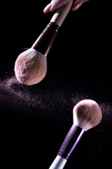 Two makeup brushes against a dark background, with a scattering of what appears to be cosmetic...