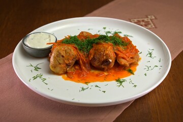 Traditional stuffed cabbage rolls served with tomato sauce, fresh dill, and a side of sour cream on a white plate.