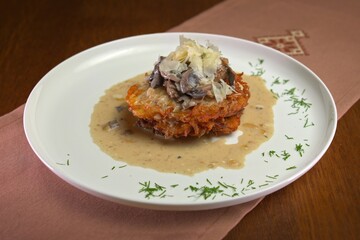 Crispy potato pancakes topped with creamy mushroom sauce and shaved cheese, garnished with fresh dill on a white plate.