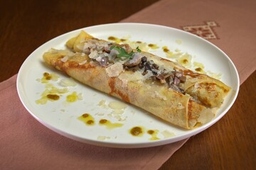 Savory crepes stuffed with mushrooms and topped with grated cheese, herbs, and a light drizzle of oil on a white plate.