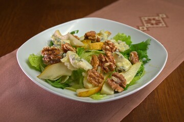 Fresh salad with pear slices, blue cheese, and walnuts on a bed of mixed greens, served in a white bowl.