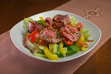 Fresh Asian-style beef salad with sliced rare steak, bell peppers, cucumbers, cherry tomatoes, and...