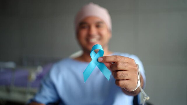 Close up at hand showing blue ribbon of smiling young patient man with prostate cancer in the recovery room at hospital, supporting protection for cancer and health awareness on world cancer day.