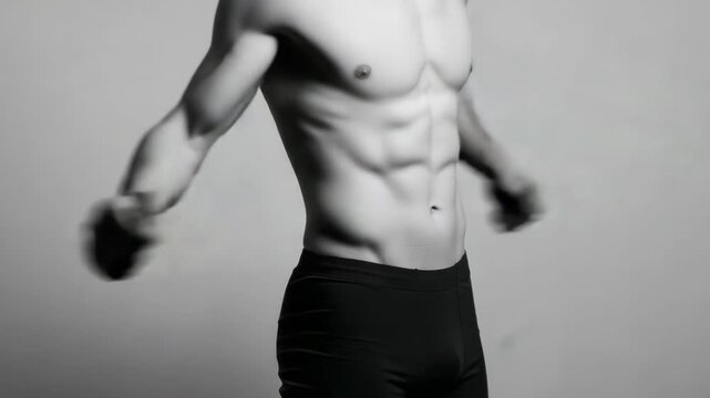 A mans muscular torso with defined abs and arms, wearing dark briefs, captured in a black and white studio portrait