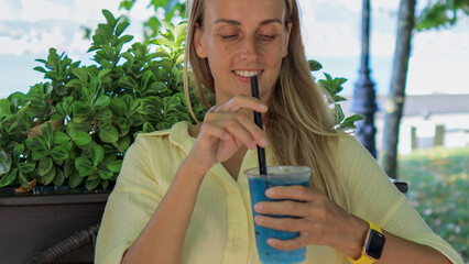 Smiling Woman Stirring Iced Blue Matcha Tea Outdoors