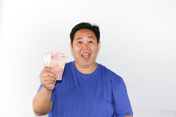 Cheerful asian guy holding a lot of money with winning gesture,  indonesian rupiah, bank notes