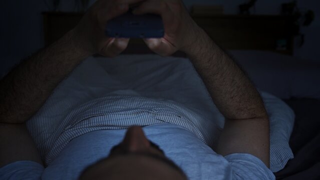 Smartphone and social network addiction concept. Young male using smartphone in bed at night