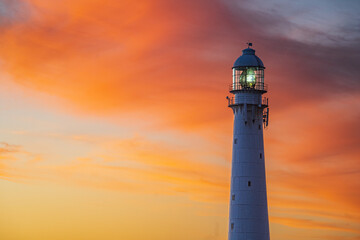 Scenic lighthouse at sunset with warm golden light, dramatic clouds, and a tranquil ocean horizon. Perfect for travel, tourism, and maritime themes, with ample copy space for text placement. Ideal as 