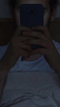 Smartphone and social network addiction concept. Young male using smartphone in bed at night