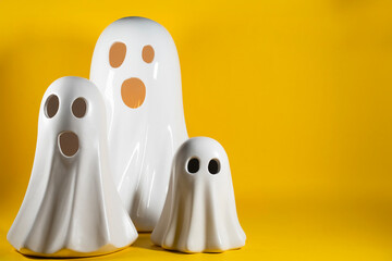 Halloween family concept. Three white ghost toy figurines over yellow background with copyspace