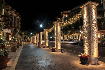 Nighttime street scene featuring decorative concrete pillars adorned with festive garlands in a resort area.