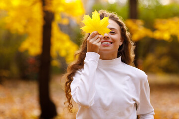 Young woman holds yellow leaf in her hand with smile in the park at sunset