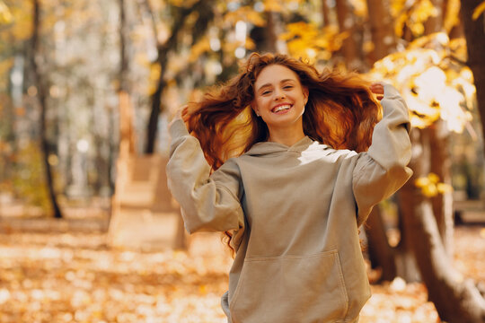 Smiling young woman with curly hairstyle enjoys the autumn weather in the forest with the yellow leaves at sunset - Powered by Adobe