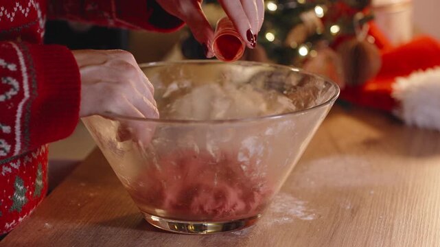 Woman Sprinkling Red Powder into Dough Bowl Near Christmas Tree While Preparing Festive Holiday Cookies