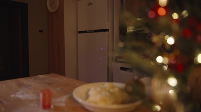 Blurred Woman Holding Dough in Bowl Behind Christmas Tree with White Dough and Red Powder on Table