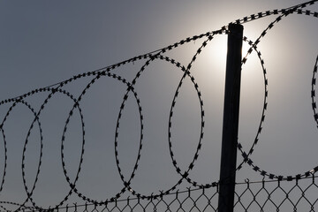 fencing barbered wire and mesh at sunset, barbed wire on prison wall, dark sky