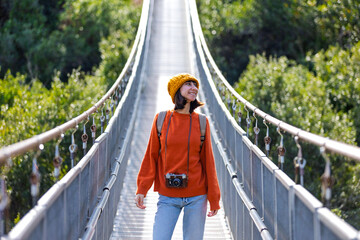 Travel and photography. A young woman with a camera and a backpack walks along a suspension bridge....
