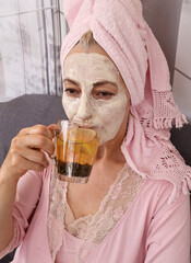 A woman wearing a cosmetic mask on her face drinks herbal tea.