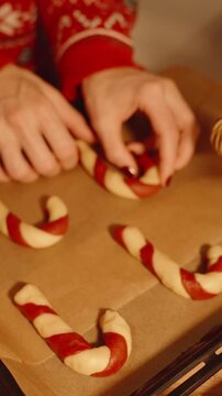 Vertical video. Woman Arranging Raw Candy Cane Cookies Evenly on Tray with Christmas Tree in Background