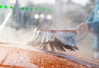 Close-up of Car wash process in a bright and sunny location with foam and driver using a brush to...