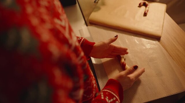 Woman Rolling Dough with Both Hands on Textured Mat beside Parchment and Wooden Board during Christmas Season