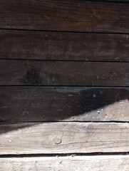 Dark brown wooden planks with dirt splashes, partially in shadow. Dark background.